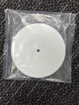 Round white object with a black dot in a clear plastic bag on a textured surface