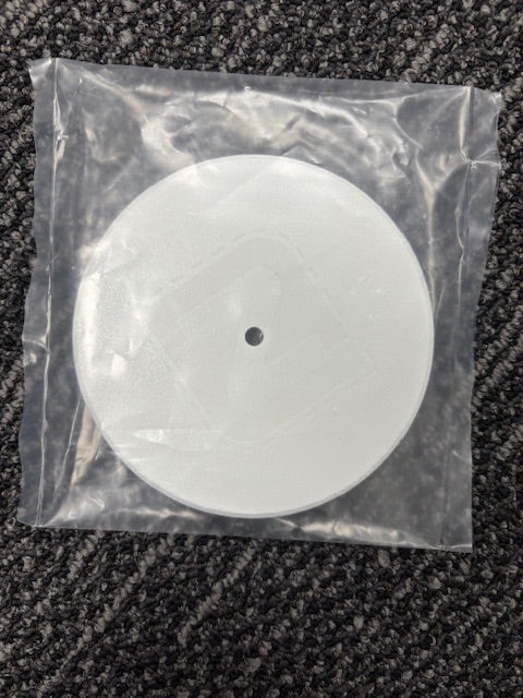 Round white object with a black dot in a clear plastic bag on a textured surface